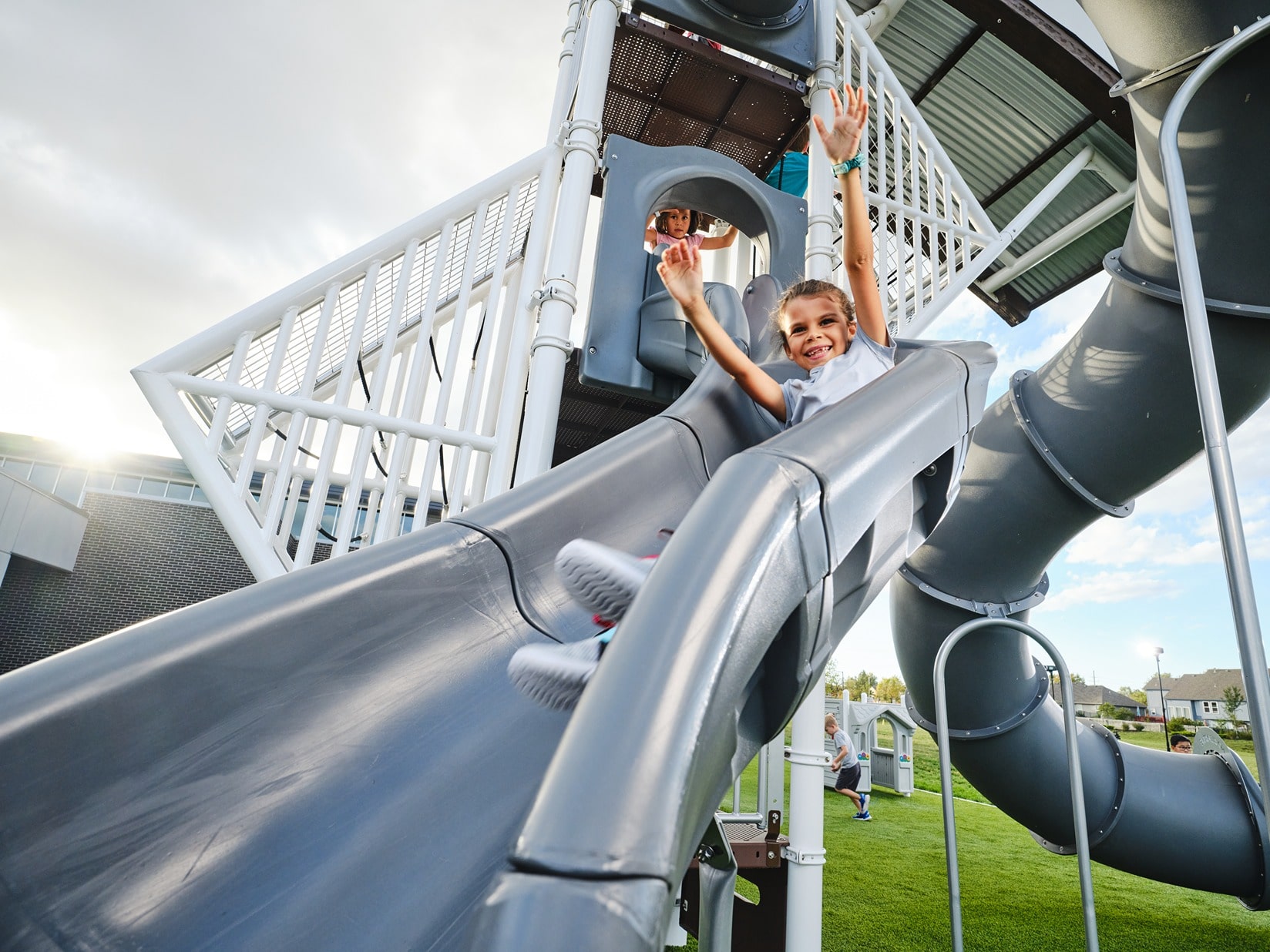 Child going down a slide with his hands in the air.